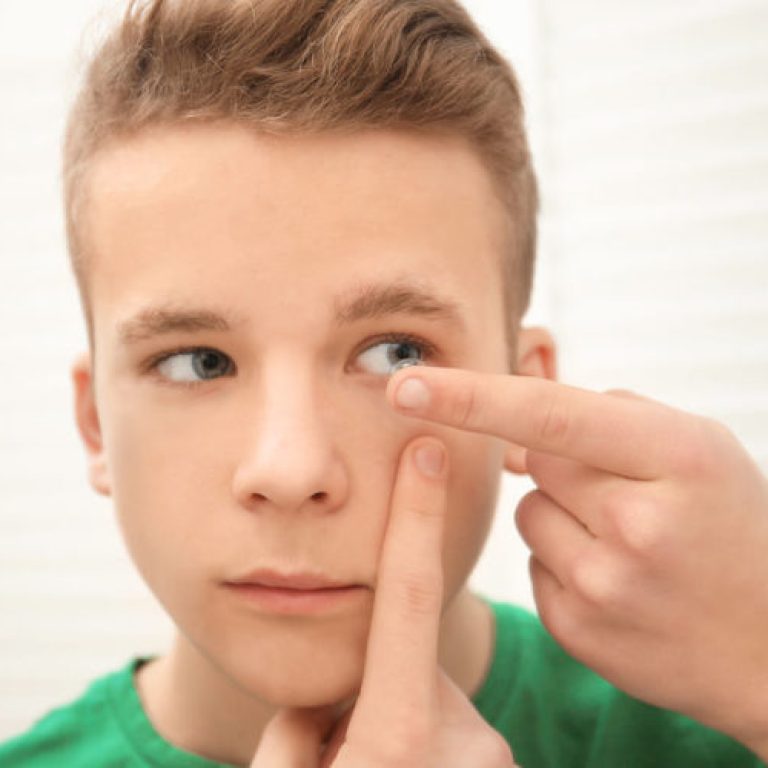 Teenage boy putting contact lens in his eye indoors